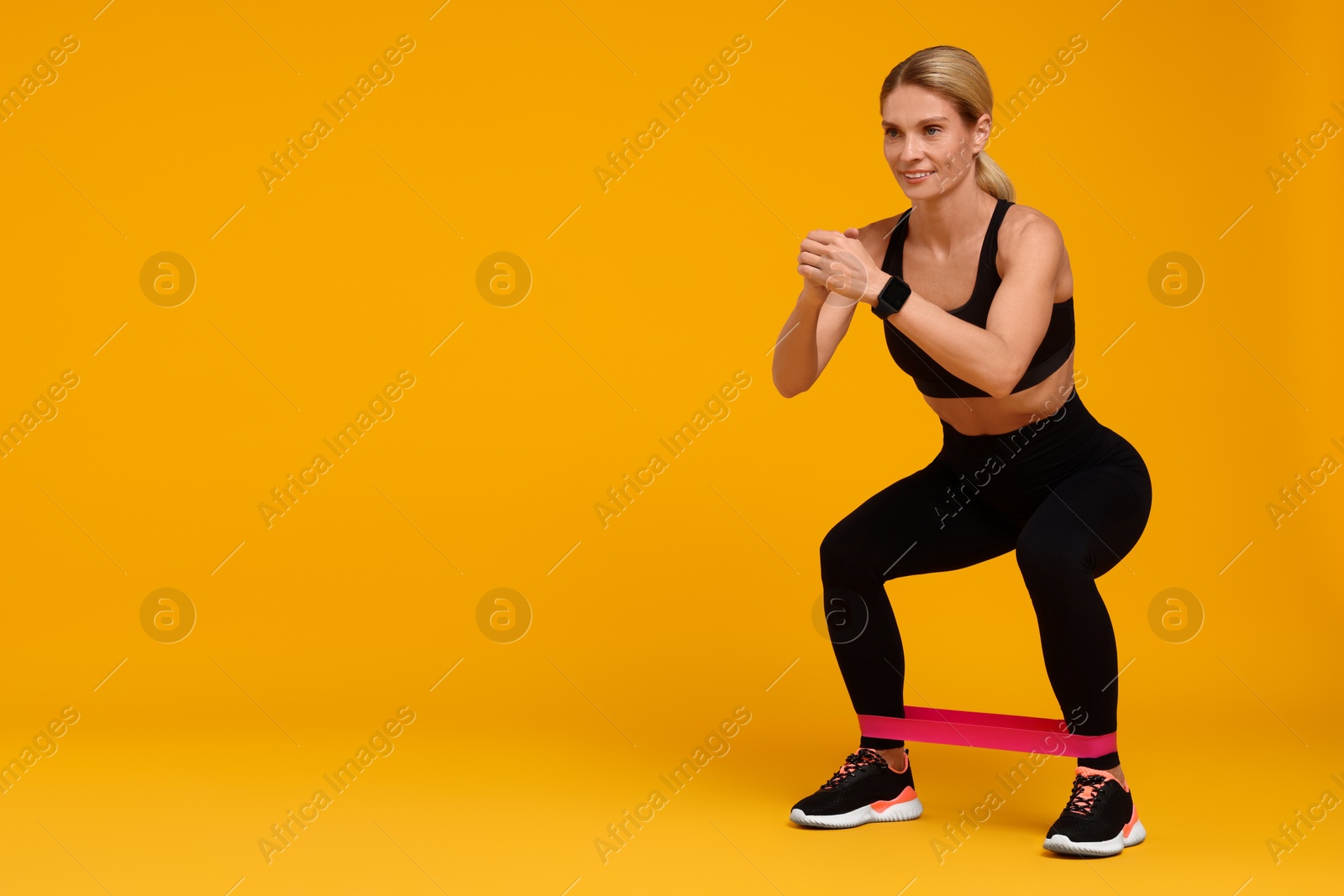 Photo of Woman exercising with elastic resistance band on orange background. Space for text