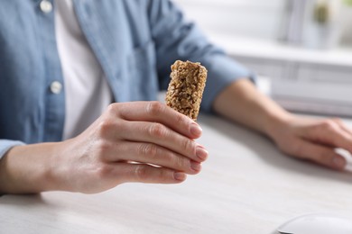 Woman holding tasty granola bar at light table indoors, closeup