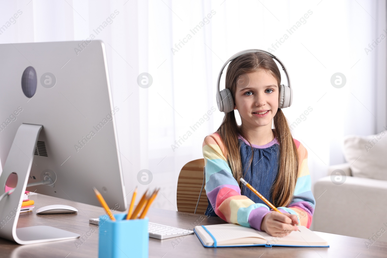 Photo of E-learning. Cute girl taking notes during online lesson at table indoors