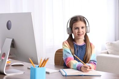 E-learning. Cute girl taking notes during online lesson at table indoors