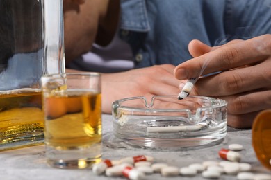 Photo of Alcohol and drug addiction. Man with smoldering cigarettes, whiskey and pills at grey table, selective focus