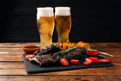 Photo of Glasses of beer, tasty fried ribs, grilled corn and sauce on wooden table, closeup