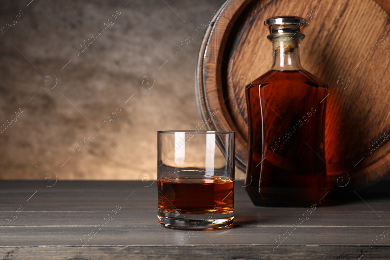 Photo of Barrel, bottle and glass of tasty whiskey on wooden table, space for text