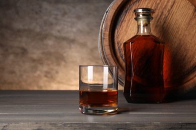 Photo of Barrel, bottle and glass of tasty whiskey on wooden table, space for text