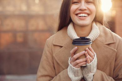 Young woman with cup of coffee on city street in morning, closeup