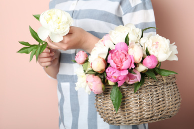 Photo of Woman with bouquet of beautiful peonies in basket on beige background, closeup