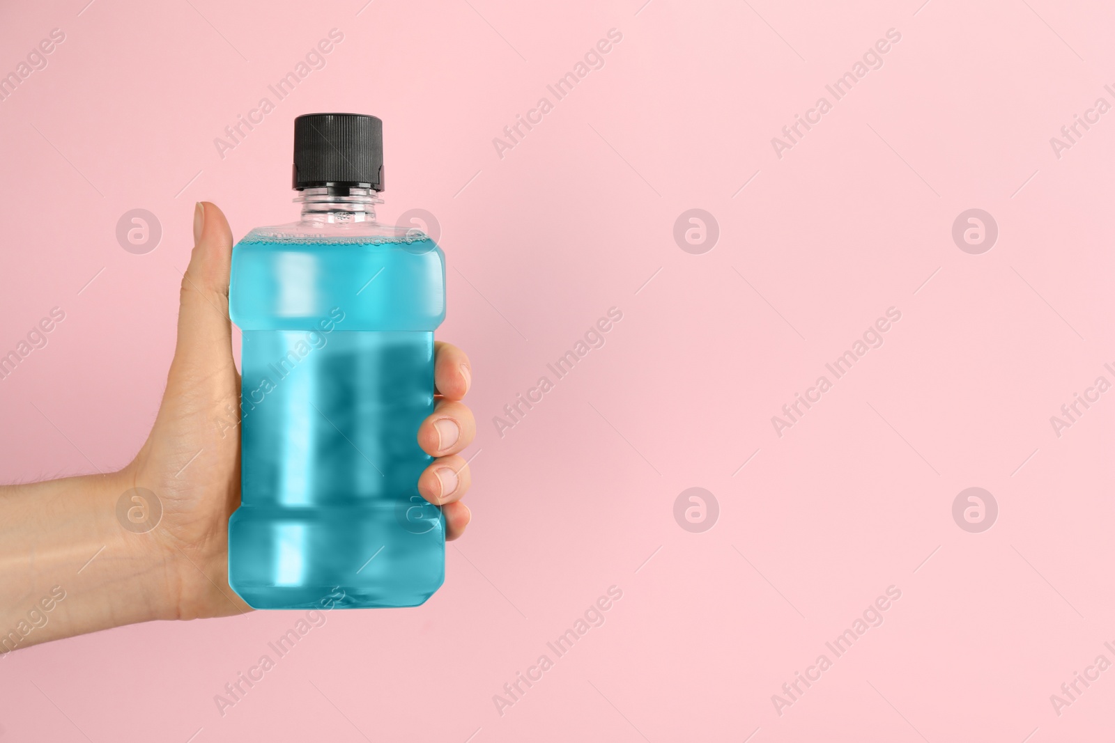 Photo of Woman holding bottle with mouthwash on pink background, closeup. Space for text