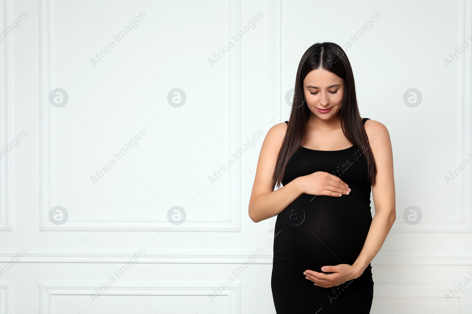 Photo of Beautiful pregnant woman in black dress near light grey wall, space for text