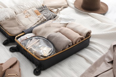 Photo of Open suitcase with folded clothes, shoes and accessories on bed
