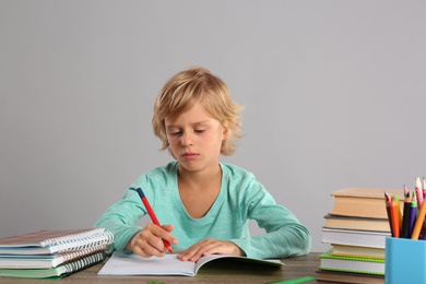 Little boy doing homework at table on grey background