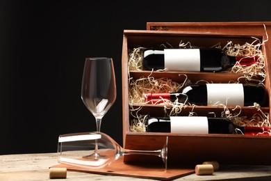 Box with wine bottles, corks and glasses on wooden table against black background