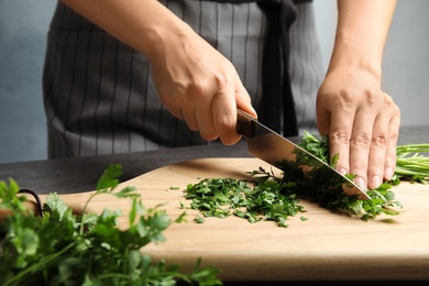 Photo of Woman cutting fresh green parsley on wooden board, closeup