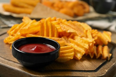 Photo of Tasty ketchup and ridged chips on wooden board, closeup