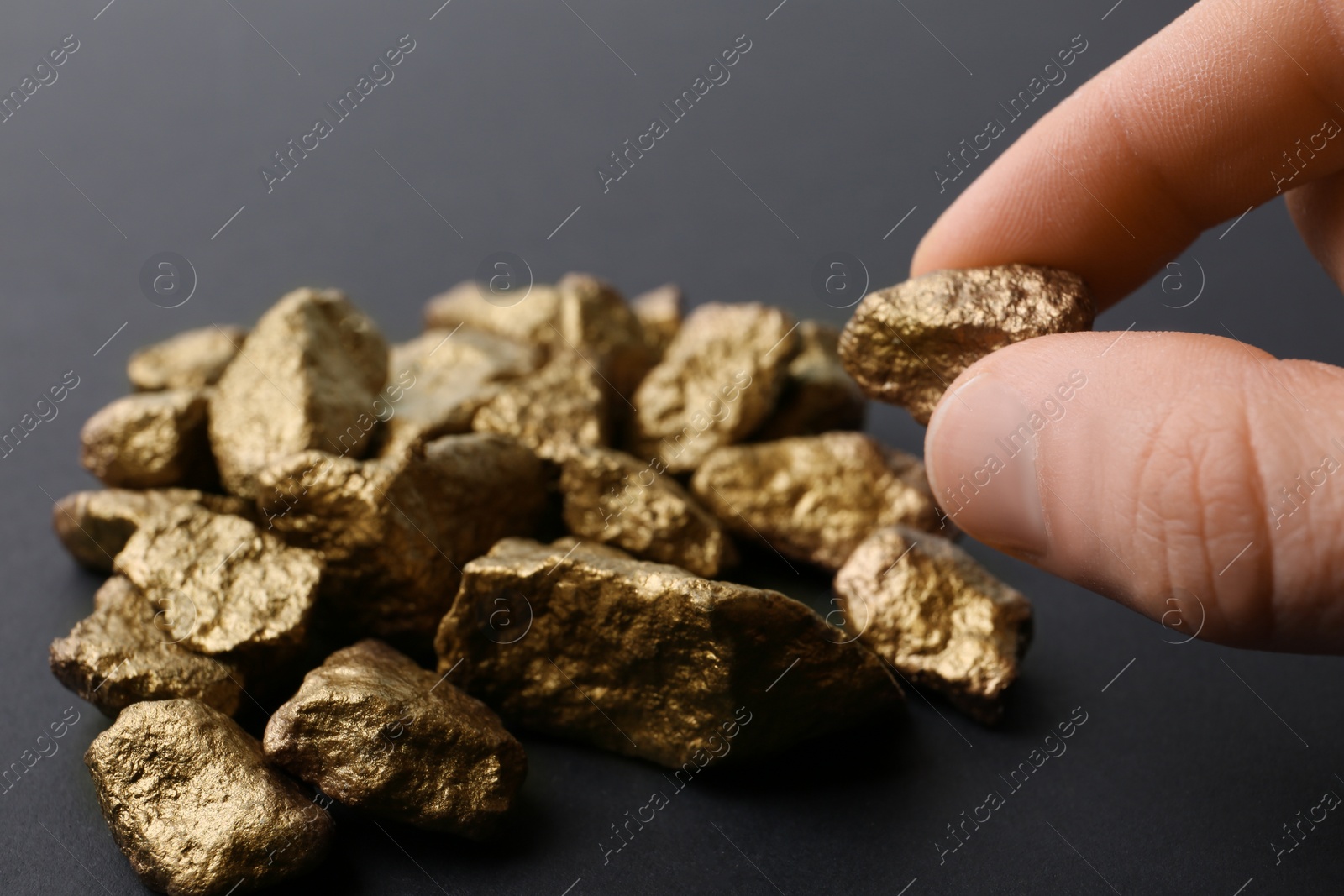 Photo of Man taking gold nugget from pile on dark background, closeup