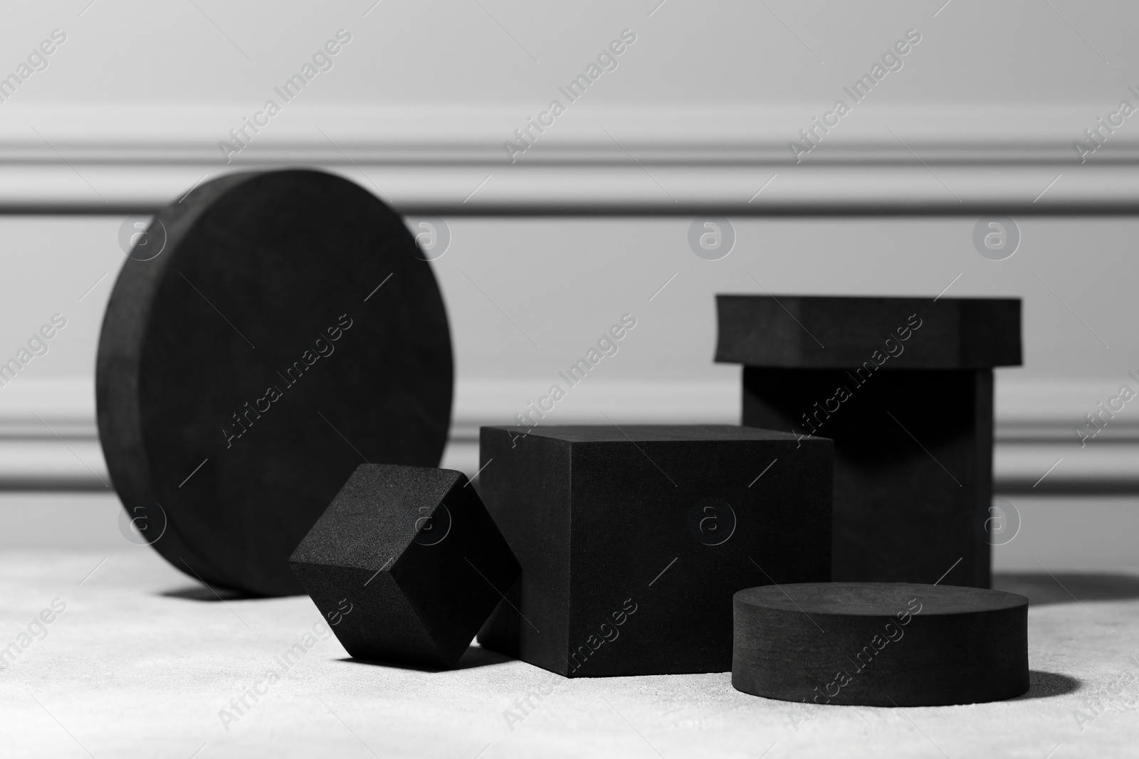 Photo of Black geometric figures on light grey table. Stylish presentation for product