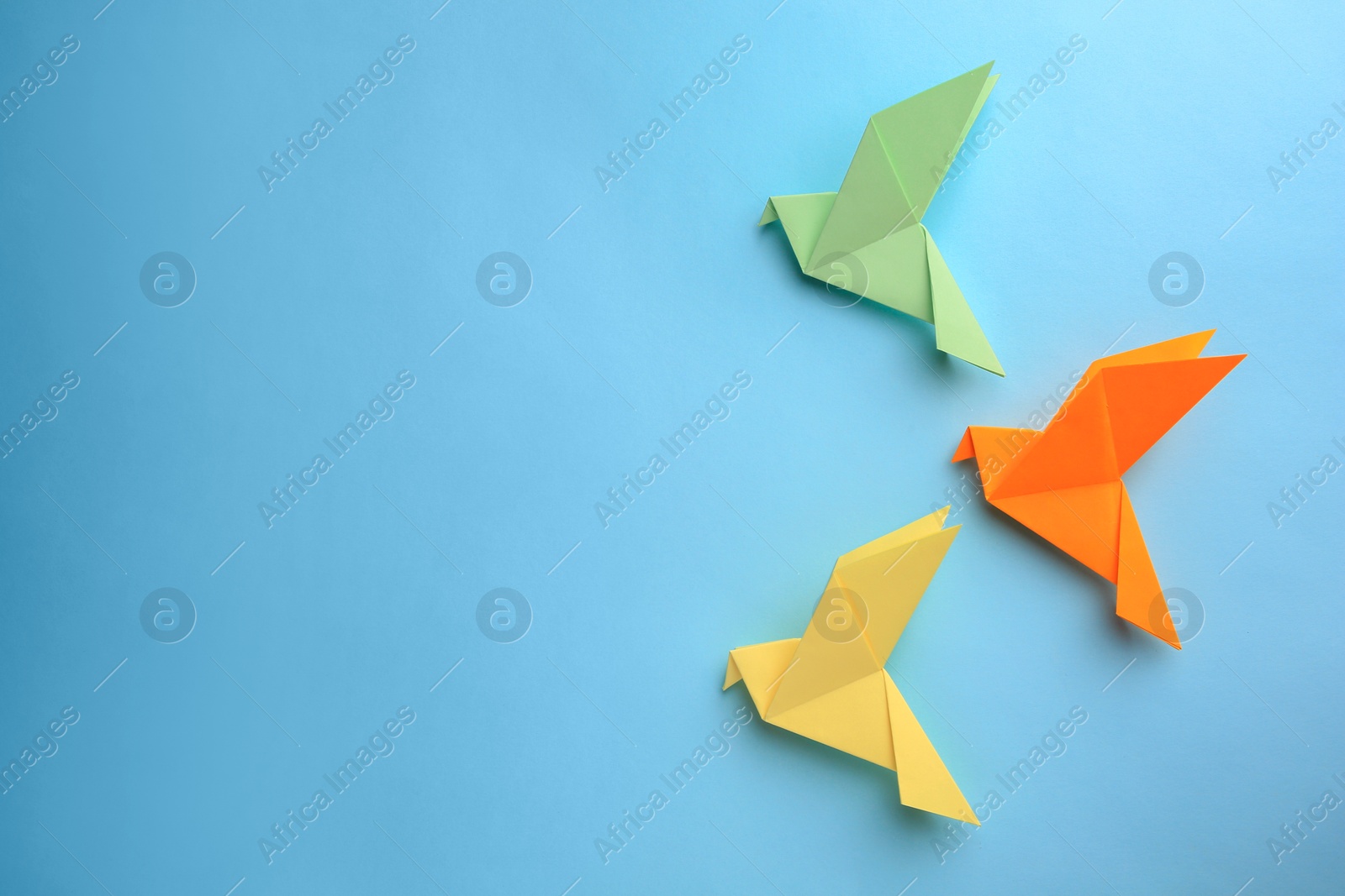 Photo of Origami art. Colorful handmade paper birds on light blue background, flat lay. Space for text