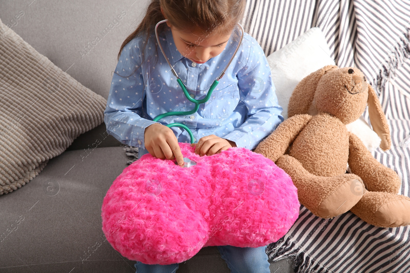 Photo of Cute child imagining herself doctor while playing with stethoscope on sofa in living room