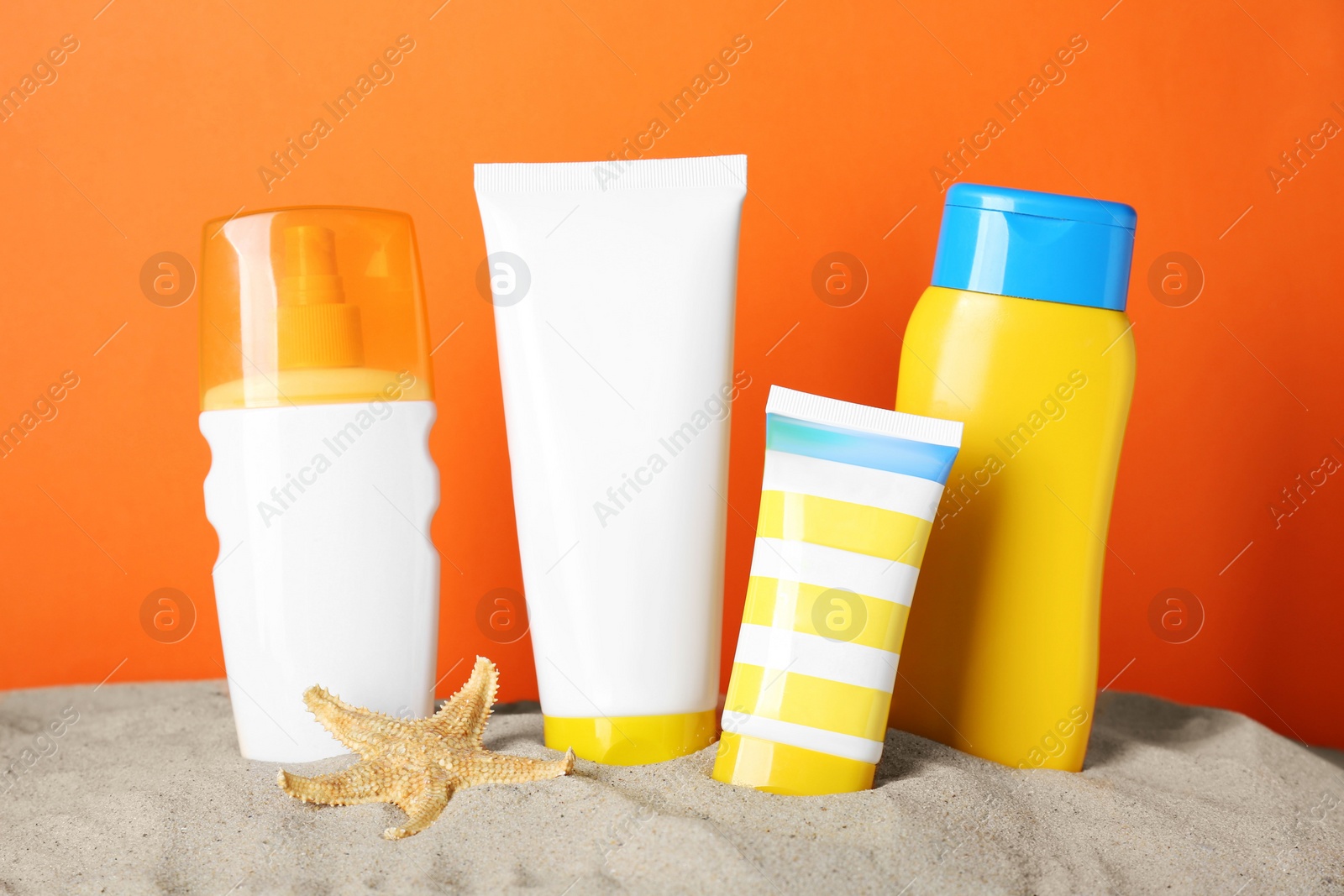 Photo of Different suntan products and starfish on sand against orange background