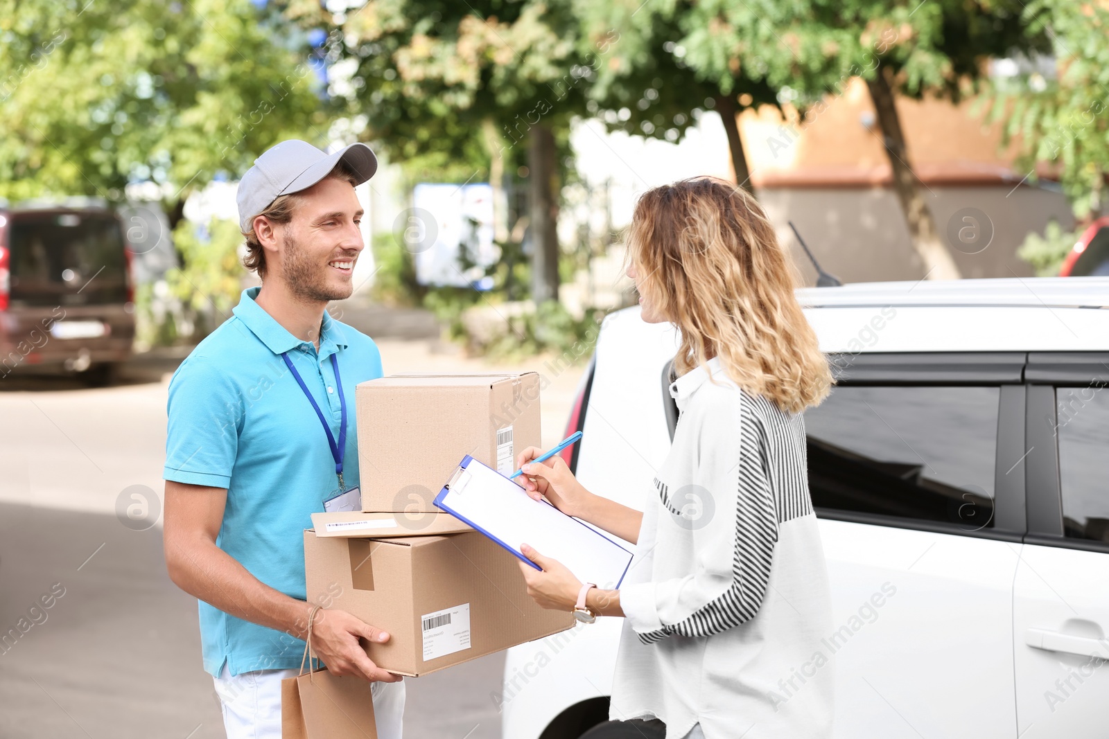 Photo of Young woman signing documents after receiving parcels from courier outdoors