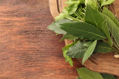 Aromatic fresh bay leaves and different herbs on wooden table, top view. Space for text