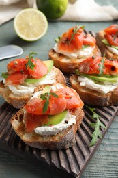 Photo of Delicious sandwiches with cream cheese, salmon, avocado and arugula on light blue wooden table, closeup