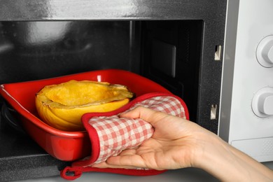 Photo of Woman taking baked spaghetti squash outmicrowave oven, closeup
