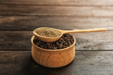 Spoon with powdered black pepper and corns in bowl on wooden table