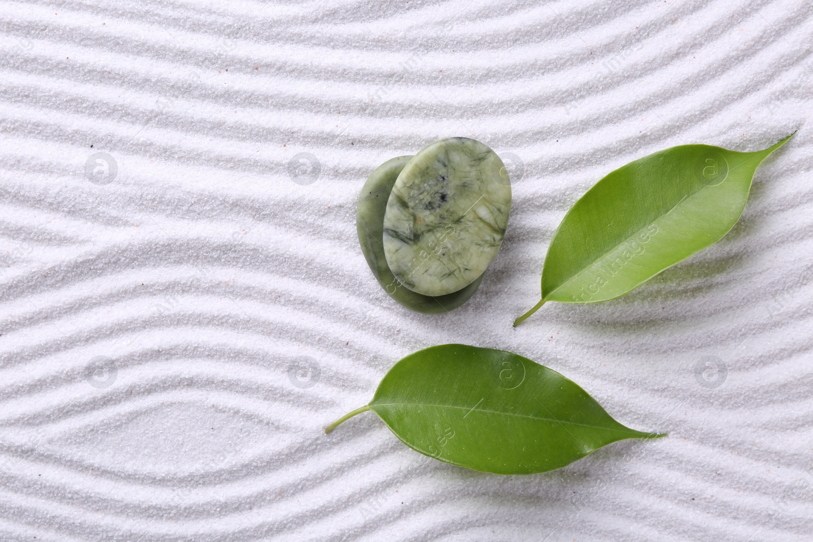 Photo of Zen garden stones and green leaves on white sand with pattern, flat lay