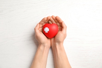 Photo of Man holding red heart with adhesive plasters on wooden background, top view. Cardiology concept