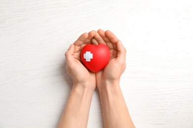 Man holding red heart with adhesive plasters on wooden background, top view. Cardiology concept