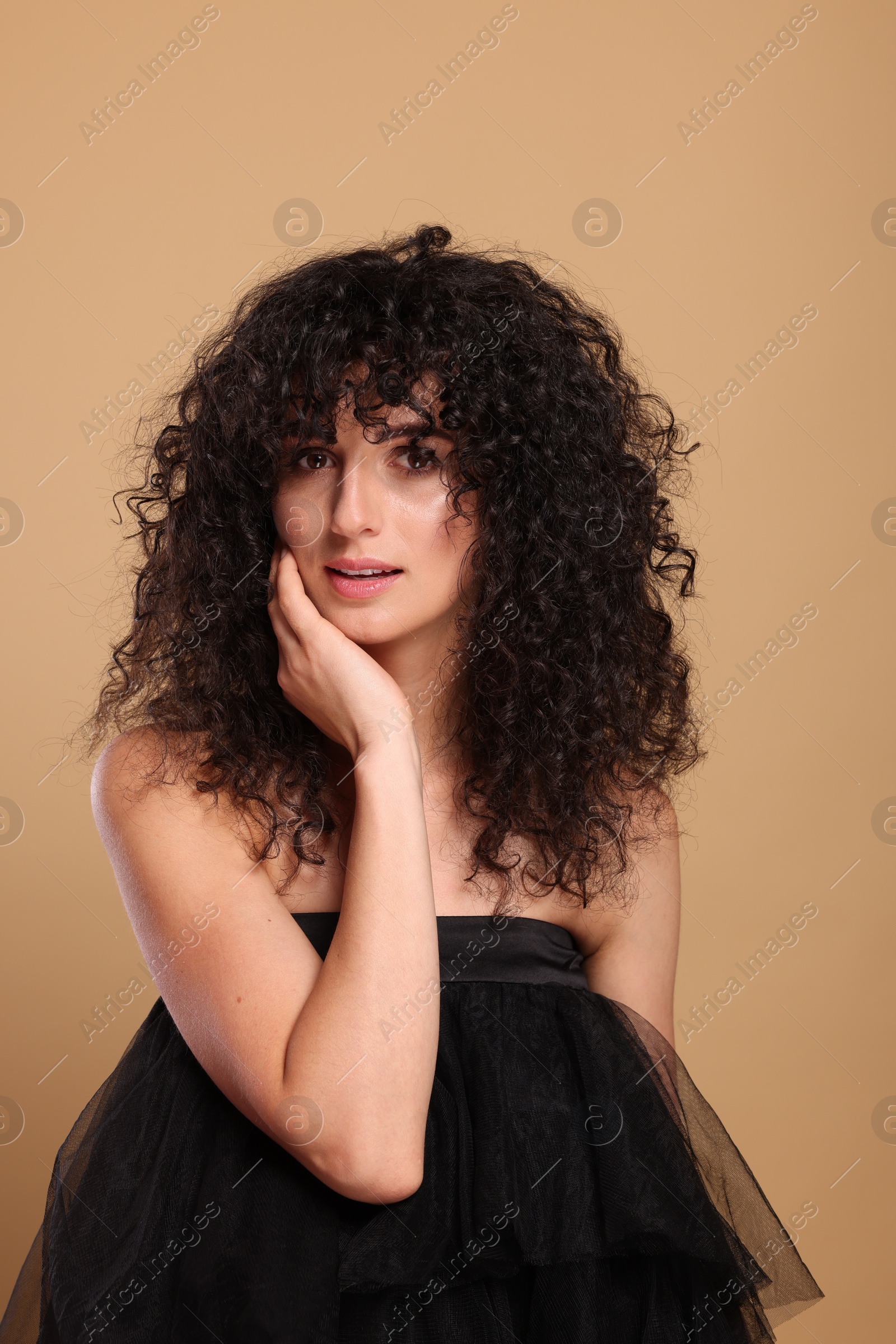 Photo of Beautiful young woman with long curly hair on beige background