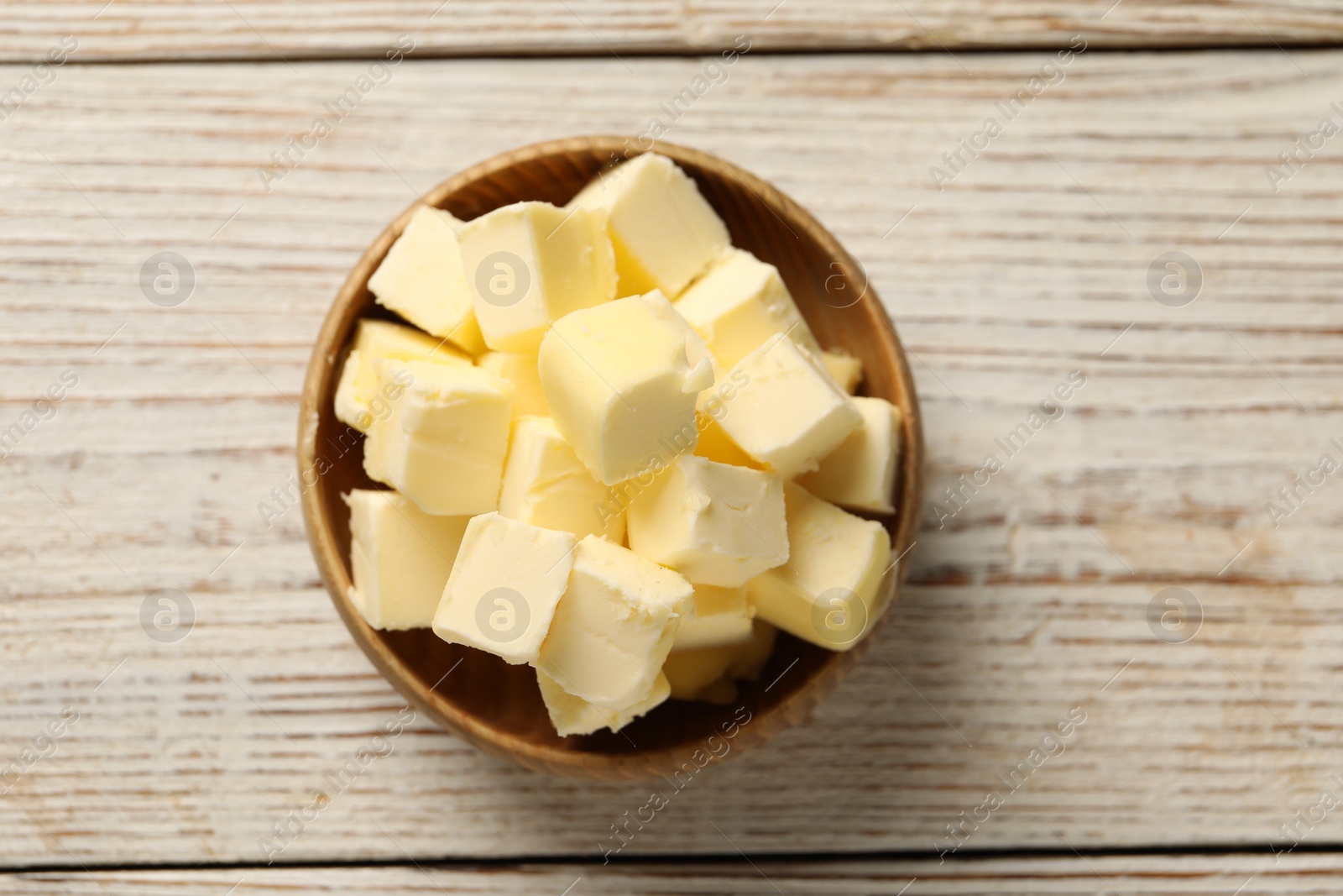 Photo of Tasty butter cubes in bowl on light wooden table, top view