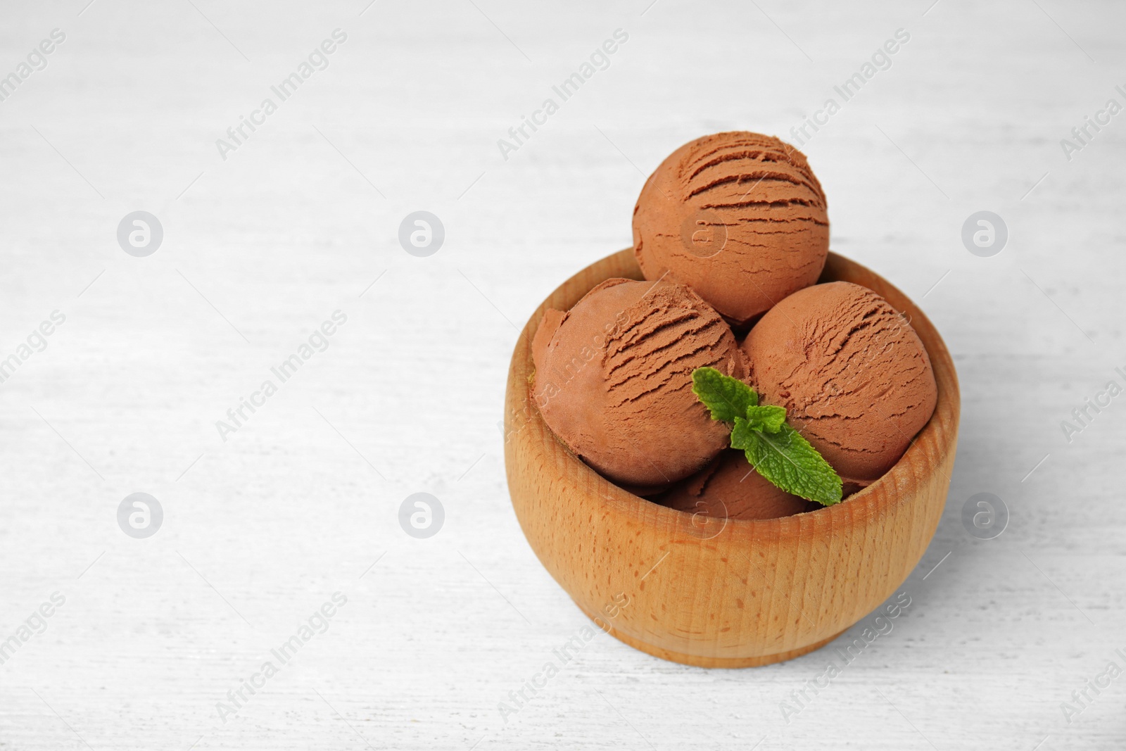Photo of Wooden bowl of chocolate ice cream on white table, space for text