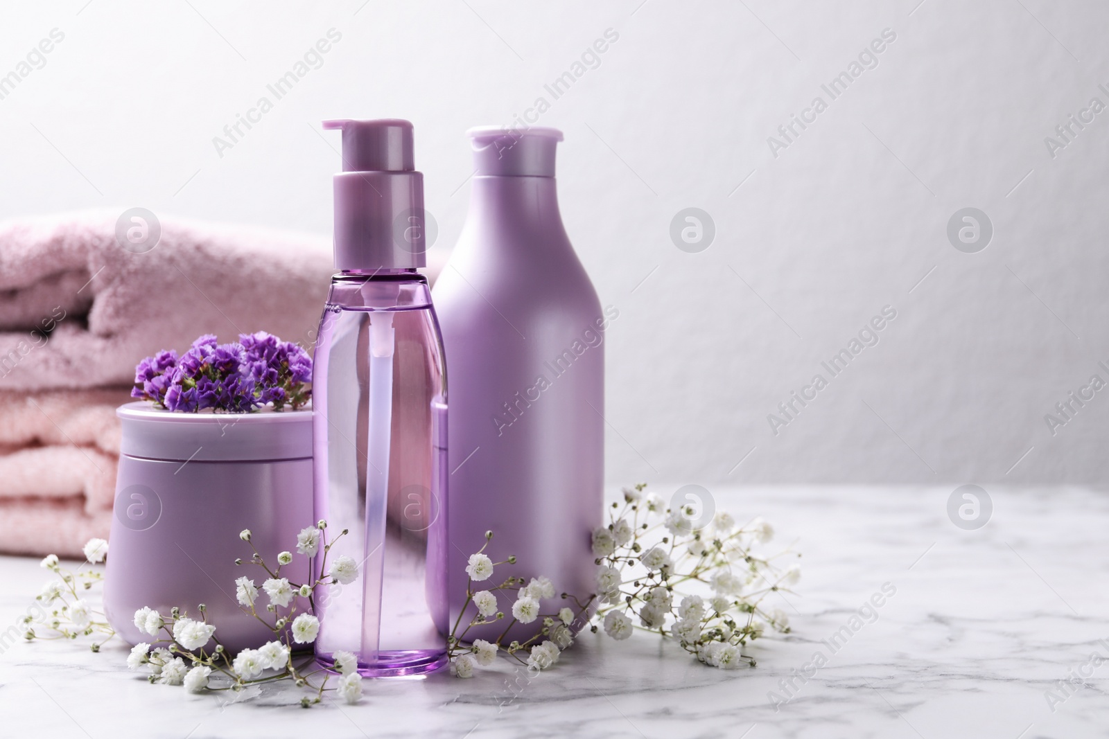 Photo of Set of hair cosmetic products and flowers on white marble table. Space for text