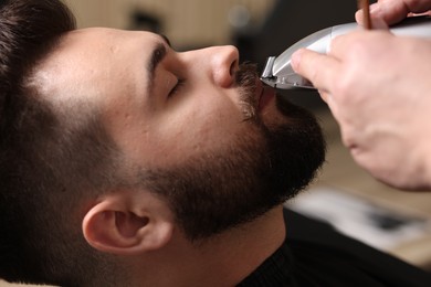 Photo of Professional barber trimming client's mustache in barbershop, closeup