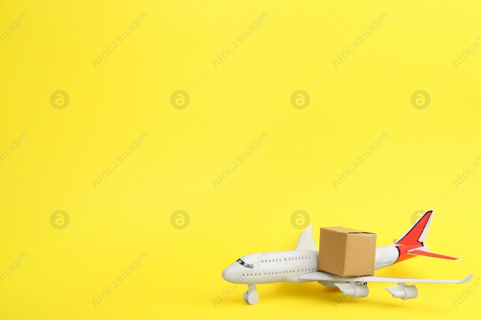 Photo of Airplane model and carton box on yellow background, space for text. Courier service