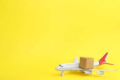 Airplane model and carton box on yellow background, space for text. Courier service