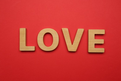 Photo of Word LOVE made of wooden letters on red background, flat lay
