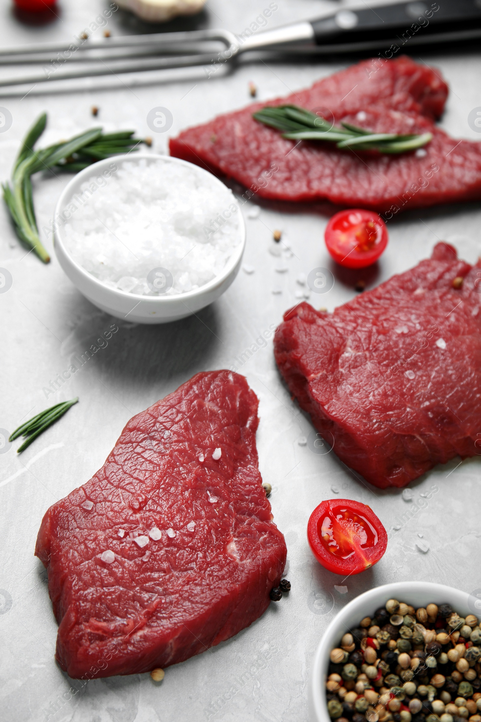 Photo of Fresh raw meat steaks and spices on light grey table