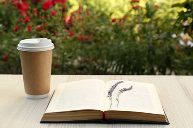 Photo of Open book with paper cup of coffee and dried flowers on wooden table in garden
