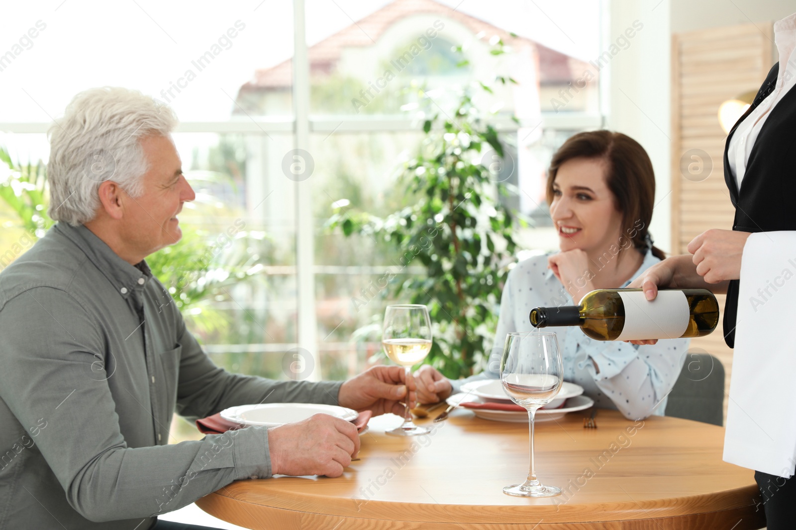 Photo of Waitress pouring wine into glass for customers in restaurant