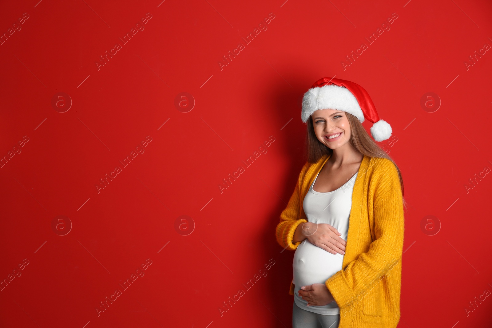 Photo of Young pregnant woman in Santa hat on red background, space for text. Christmas celebration
