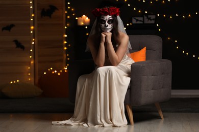 Photo of Young woman in scary bride costume with sugar skull makeup against blurred lights indoors. Halloween celebration