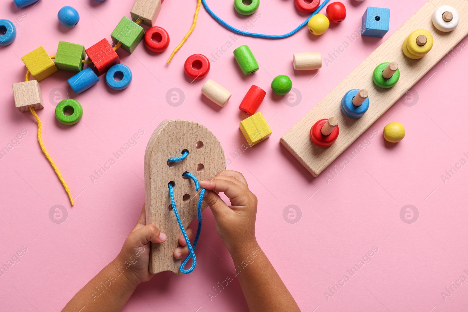 Photo of Motor skills development. Little child playing with wooden lacing toy at pink table, top view