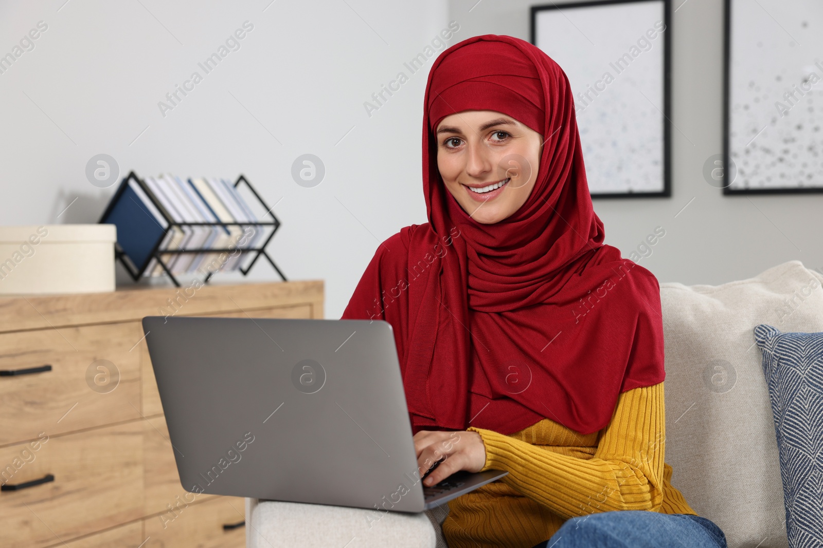 Photo of Muslim woman using laptop at couch in room