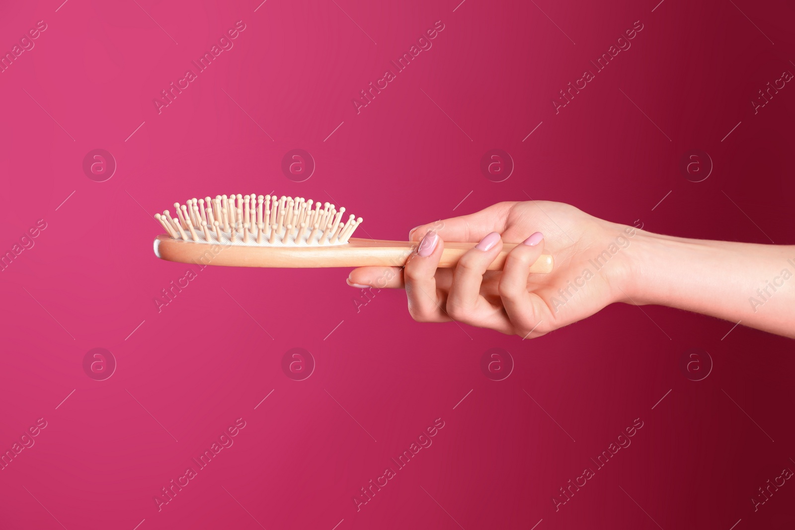 Photo of Woman holding wooden hair brush against crimson background, closeup