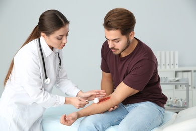 Female doctor cleaning young man's arm injury in clinic. First aid