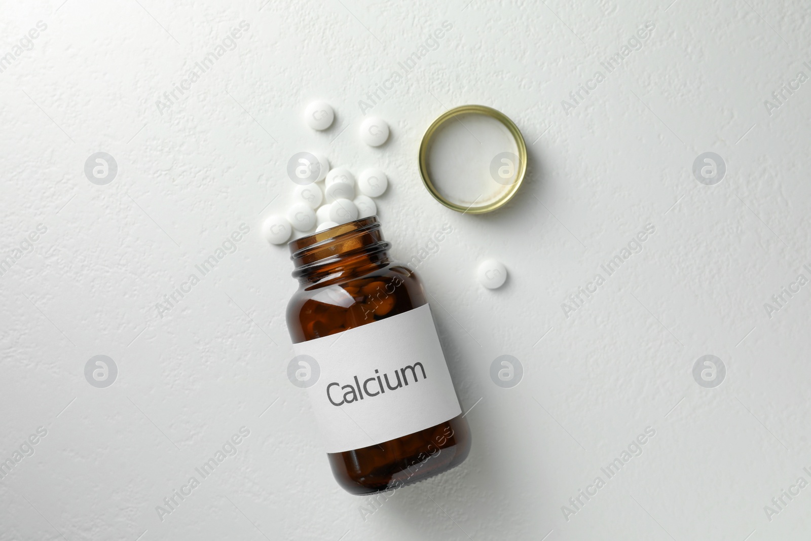 Photo of Overturned bottle of calcium supplement pills on white table, flat lay