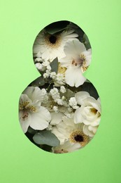 Photo of View of beautiful flowers through number 8 shaped hole in green paper. International Women's day