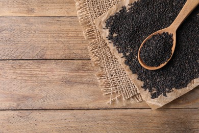 Black sesame seeds and spoon on wooden table, flat lay. Space for text